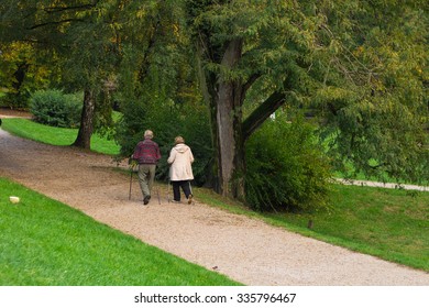 Senior Citizen Couple Walking In The Park With Nordic Walking Poles. 