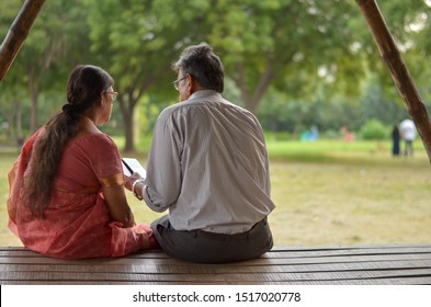 Senior Citizen Indian Man Reads From Mobile Phone Sitting With His Wife In A Park In New Delhi, India. Concept Love