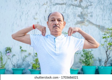 Senior Citizen Or An Old Indian Man Performing Yoga Early Morning, In His Terrace In White Tshirt And Pants. Stay Home Stay Safe And Fit