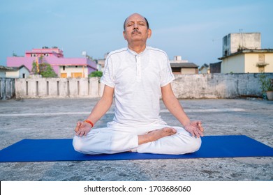 Senior Citizen or an Old Indian Man Performing Yoga Early Morning, in his Terrace in white Tshirt and Pants. Stay Home Stay Safe and Fit - Powered by Shutterstock