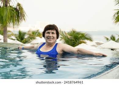 Senior citizen woman relaxes in the infinity pool. Portrait of a retired woman on vacation in swimsuit. woman smiles and looks at the camera. - Powered by Shutterstock