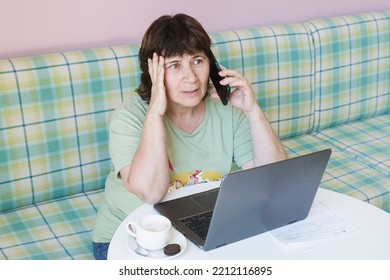 Senior citizen woman at a table with a laptop talking on a mobile phone. Mature female freelancer works in a cafe. Woman discussing problems on the phone and holding her head - Shutterstock ID 2212116895