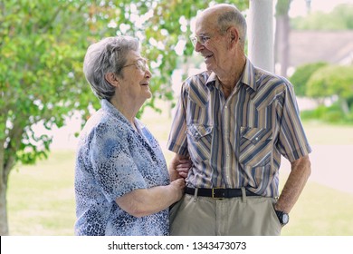 Senior Citizens Talking And Smiling Together While Outdoors On A Porch In Delcambre, Louisiana. Octogenarian Couple Happy And In Love After 70 Years Of Marriage. Two Older Happy Adults Now Seniors.