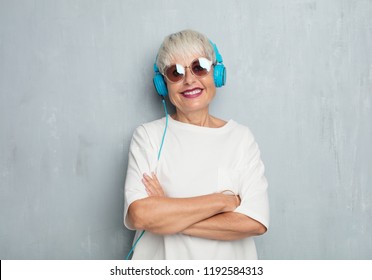 senior cool woman with headphones, listening music against grunge cement wall.