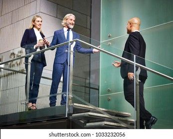 senior corporate executive welcoming visitor on stair of modern office building, low angle view.