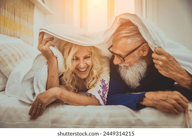 Senior couple in the 60's having fun at home, they are playing in bed - Cheerful married couple portrait, concepts about senority and relationship - Powered by Shutterstock