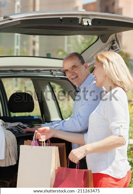 Senior couple with bags near car at shopping center\
parking lot