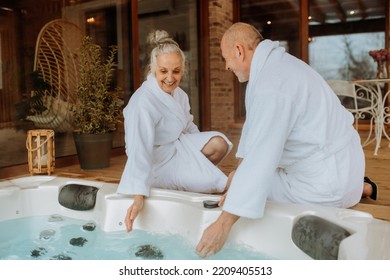 Senior couple in bathrobe checking temperature in outdoor hot tub, preparing for bathing with his wife. - Powered by Shutterstock