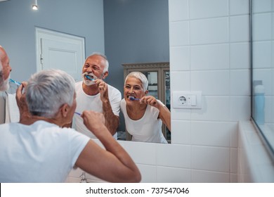 A senior couple brushing their teeth in a brightly lit living bathroom in the morning. - Powered by Shutterstock