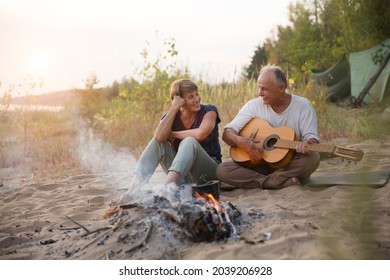 Senior couple Camping holiday in the summer nature. Camping concept. senior man playing guitar and singing song to his wife sitting on the beach near the fire
 - Powered by Shutterstock