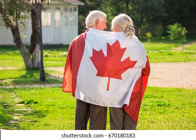 Senior Couple And Canadian Flag. Two Elderly People, Back View. Love To Homeland.