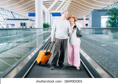 Senior couple carrying a luggage while using a smartphone with happy expression on the escalator of airport terminal - Powered by Shutterstock