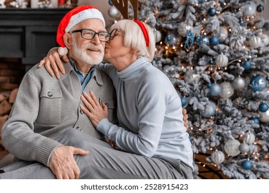 Senior couple celebrating christmas at home and elderly woman kissing her husband. Old spouses grandparents embracing hugging cuddling together for New Year celebration - Powered by Shutterstock