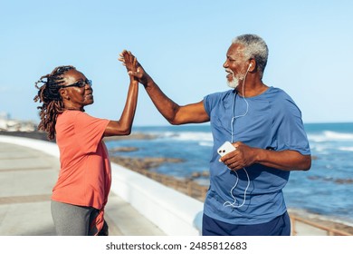 Senior couple celebrating fitness achievements with a high five by the seaside. Active and happy elderly exercising outdoors by the ocean. - Powered by Shutterstock