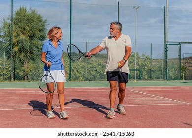 senior couple chats animatedly while walking to the tennis court, excited to start their match. Their conversation reflects camaraderie, showcasing their active lifestyle and passion for tennis - Powered by Shutterstock