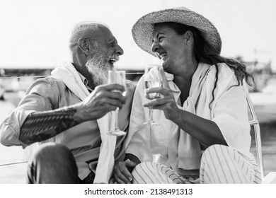 Senior Couple Cheering With Champagne On Boat During Summer Vacation - Focus On Right Woman Face - Black And White Editing