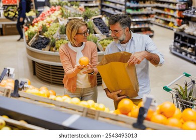 Senior couple choosing fresh oranges from grocery store produce section putting them in paper bag, shopping for healthy food - Powered by Shutterstock