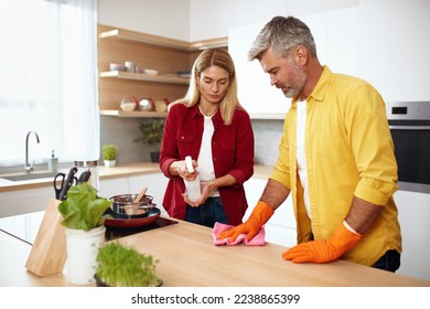 Senior Couple Cleaning Table. Caring Guy And His Wife Wiping Crumbs from Wooden Kitchen Table Together. Mature People Using Household Cleaner Wipe for Cleaning - Powered by Shutterstock