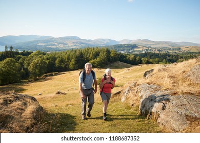 Senior Couple Climbing Hill On Hike Through Countryside In Lake District UK Together