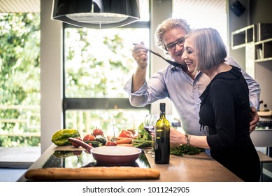 Senior Couple Cooking Healthy Food And Drinking Red Wine At House Kitchen