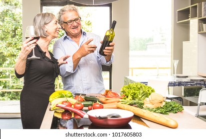 Senior couple cooking healthy food and drinking red wine at house kitchen - Retired people at home preparing lunch with fresh vegetables and bio products - Happy elderly concept with mature pensioner - Powered by Shutterstock