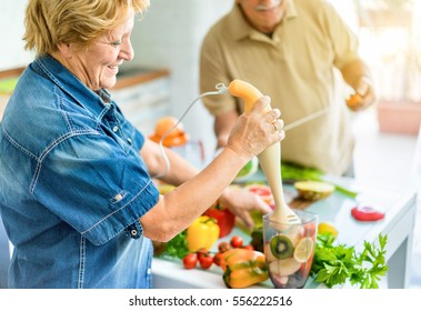 Senior Couple Cooking Healthy Vegetarian Meal With Fruits And Vegetables Together - Old Happy People Taking Care About Diet And Health - Vegan And Bio Concept - Focus On Woman Eye - Warm Vivid Filter