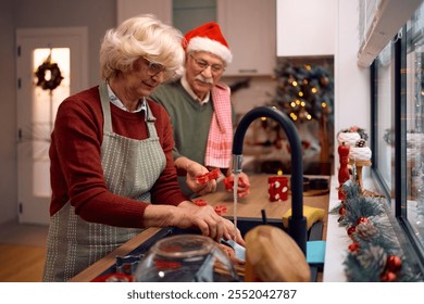 Senior couple coopering while doing the dishes after making cookies for Christmas in the kitchen. - Powered by Shutterstock