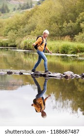 Senior Couple Crossing River Whilst Hiking In UK Lake District