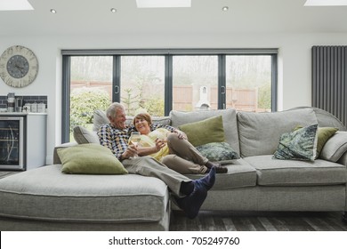 Senior couple are cuddled up on the sofa in thier home, enjoying a glass of wine.  - Powered by Shutterstock