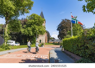 Senior couple cycling along church of Siddeburen and Groninger flag in municipallity Midden-Groningen in Groningen province in the Netherlands