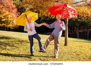 Senior couple dancing with umbrellas in a park - Powered by Shutterstock