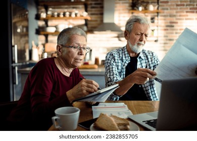 Senior couple doing bills and payments together in the kitchen at home - Powered by Shutterstock