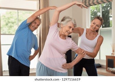 Senior Couple Doing Exercise At Home With Physiotherapist. Mature Gym Trainer Helping Elderly Man And Old Woman Exercising At Home. Retired Husband And Wife Doing Stretching Exercises At Gym.