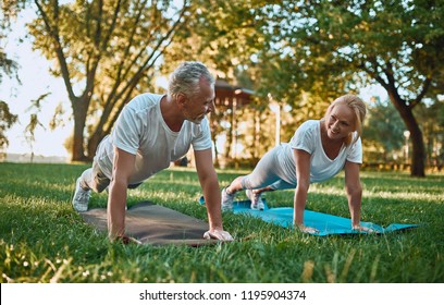 Senior Couple Is Doing Sport Outdoors. Stretching In Park During Sunrise. Doing Yoga Together. Healthy Lifestyle Concept