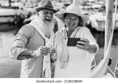 Senior Couple Doing Video Call With Mobile Phone On Sailboat During Summer Vacation - Focus On Faces - Black And White Editing