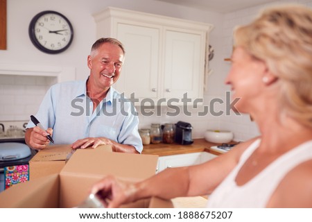 Senior Couple Downsizing In Retirement Packing And Labelling Boxes Ready For Move Into New Home