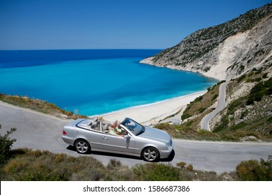 Senior Couple Driving Convertible Car Along Winding Coastal Road