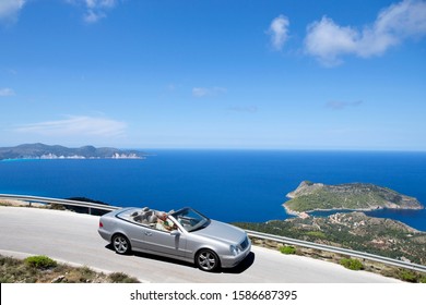 Senior couple driving convertible car along coastal road - Powered by Shutterstock