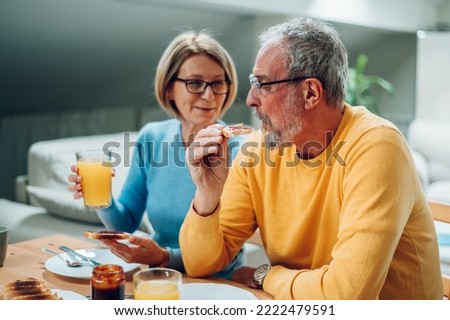 Senior couple eating breakfast at home and sitting at the table. Happy aged husband and wife enjoy spending time at home together. Focus on a mature man eating french toast. Copy space.
