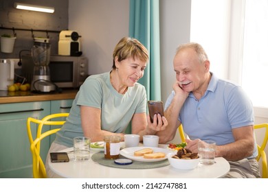 Senior couple eating breakfast and using smartphone at home. elderly couple watches news or video on a smartphone - Powered by Shutterstock