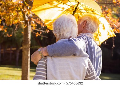 Senior couple embracing under an umbrella in a park - Powered by Shutterstock