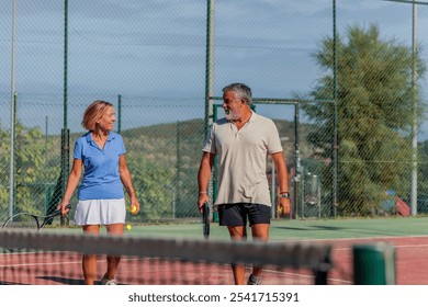 senior couple engages in conversation as they walk toward the tennis court, with the net prominently in the foreground. Their smiles reflect excitement, emphasizing their active lifestyle - Powered by Shutterstock