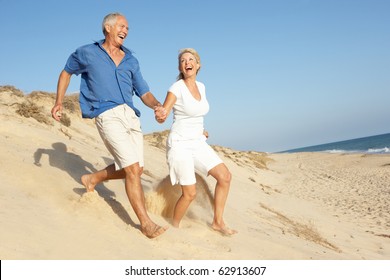 Senior Couple Enjoying Beach Holiday Running Down Dune - Shutterstock ID 62913607