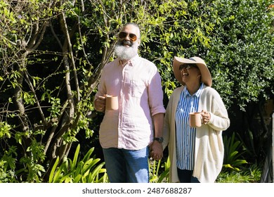 Senior couple enjoying coffee and walking in garden, smiling and holding hands. Seniors, gardening, lifestyle, happy, bonding, outdoors - Powered by Shutterstock