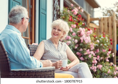 Senior couple enjoying their coffee sitting on porch in front of their house - Powered by Shutterstock