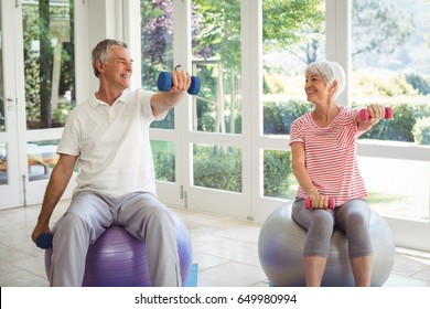 Senior Couple Exercising With Dumbbell On Exercise Ball At Home