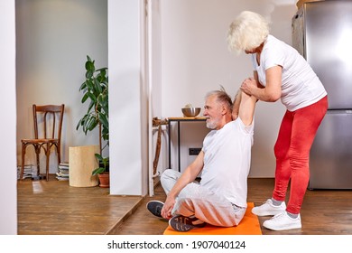 senior couple exercising at home, woman help husband to stretch, sitting on the floor. wellbeing, healthy lifestyle concept - Shutterstock ID 1907040124