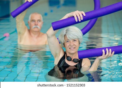 Senior Couple Exercising With Pool Noodle In Swimming Pool