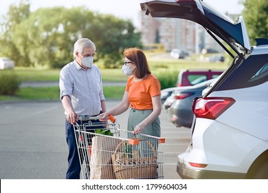 Senior Couple With Face Masks Putting Shopping In Car Outside Supermarket 