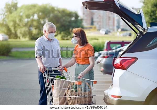 Senior couple with face masks putting shopping in car\
outside supermarket 